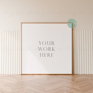 May include: A white frame with a wooden border sits on a light wood floor. The frame is against a white wall with vertical grooves. The text "YOUR WORK HERE" is printed in black on the white background inside the frame.