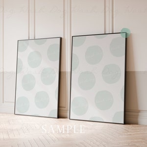May include: Two black framed posters with a white background and a light blue abstract pattern of circles. The posters are leaning against a white wall with wainscoting.