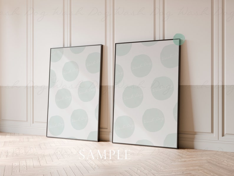 May include: Two black framed posters with a white background and a light blue abstract pattern of circles. The posters are leaning against a white wall with wainscoting.