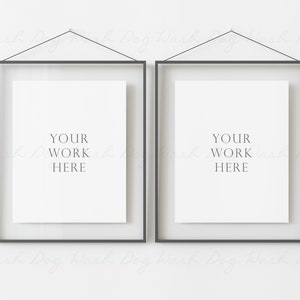 May include: Two black framed posters hanging on a white wall. The posters are blank and have the text "YOUR WORK HERE" printed on them.