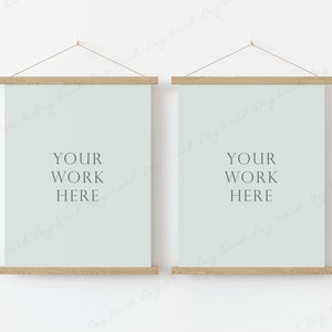May include: Two framed art prints with pale blue backgrounds and wooden hangers. Each print displays the text "YOUR WORK HERE" in a simple font. The prints are hanging on a white wall.