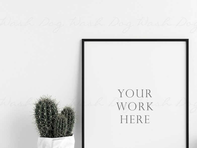 K&ouml;nnte beinhalten: Ein gerahmter Druck mit dem Text "YOUR WORK HERE" in minimalistischem Stil. Der schwarze Rahmen umgibt einen wei&szlig;en Hintergrund. Ein Topf-Kaktus mit gr&uuml;nen, stacheligen Bl&auml;ttern steht vor dem Rahmen.