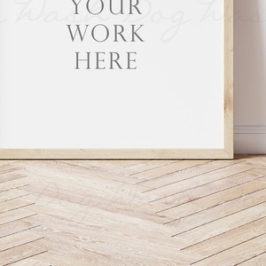 Puede incluir: Un marco de madera clara con el texto "YOUR WORK HERE" sobre un fondo blanco. El marco est&aacute; colocado sobre un suelo de madera clara con un patr&oacute;n de espiga.