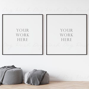 May include: Two black framed square posters with white backgrounds and the text "YOUR WORK HERE" in grey on each poster. The posters are hanging on a white wall above two grey poufs and a green plant.