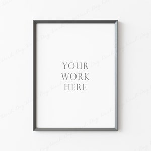 Può includere: Una cornice grigia con un passepartout bianco e il testo "YOUR WORK HERE" su una parete bianca.