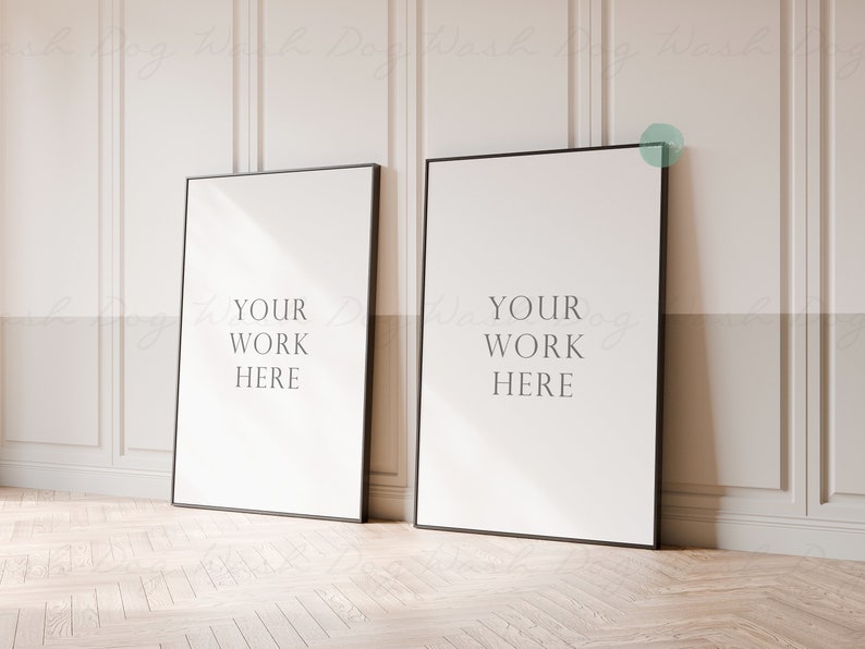 May include: Two black framed posters with white backgrounds and the text "YOUR WORK HERE" on each poster. The posters are leaning against a white wall with wainscoting.
