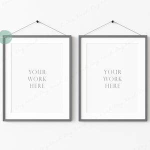 May include: Two gray picture frames hanging on a white wall. The frames are empty and have the text "YOUR WORK HERE" printed inside.