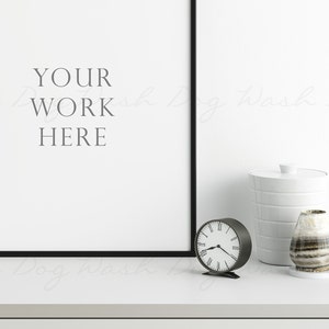 K&ouml;nnte beinhalten: Eine minimalistische Innenszene mit einem gerahmten Kunstwerk mit dem Text "YOUR WORK HERE". Eine kleine, runde Uhr, ein wei&szlig;er Beh&auml;lter und eine dekorative Vase mit Streifenmuster sind auf einer wei&szlig;en Oberfl&auml;che angeordnet.