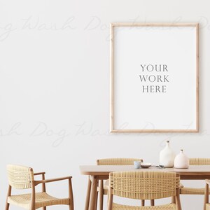 Puede incluir: Un cuadro enmarcado en madera clara con el texto "YOUR WORK HERE" colgado en una pared blanca sobre una mesa de madera con cuatro sillas de mimbre. Dos jarrones de cer&aacute;mica blanca est&aacute;n sobre la mesa.