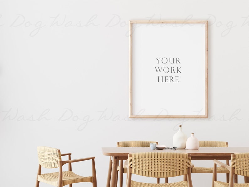 Puede incluir: Un cuadro enmarcado en madera clara con el texto "YOUR WORK HERE" colgado en una pared blanca sobre una mesa de madera con cuatro sillas de mimbre. Dos jarrones de cer&aacute;mica blanca est&aacute;n sobre la mesa.