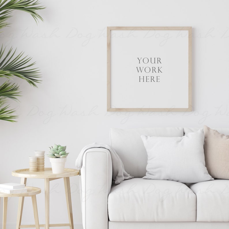 May include: A white couch with two pillows, a wooden side table with a potted succulent plant, and a framed print with the text "YOUR WORK HERE" hanging on a white wall.