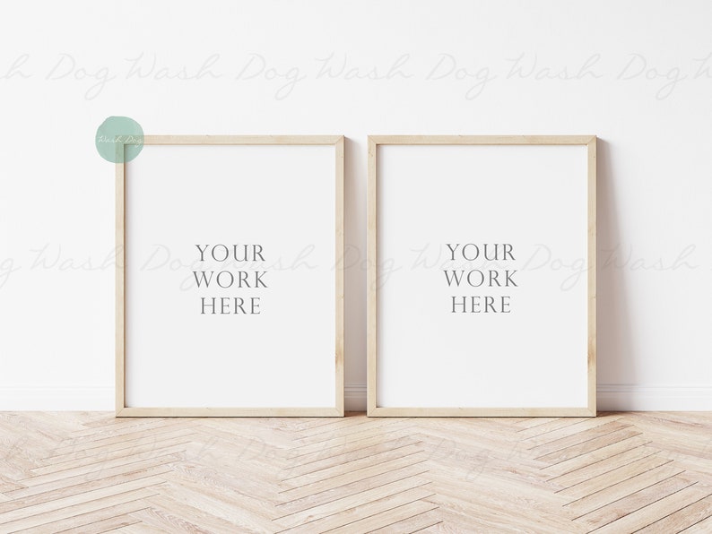 May include: Two light wood picture frames with white mats and the text "YOUR WORK HERE" in each frame. The frames are hanging on a white wall.