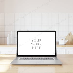 May include: A silver laptop computer with a white screen displaying the text "YOUR WORK HERE" is sitting on a light wood table in a kitchen setting.