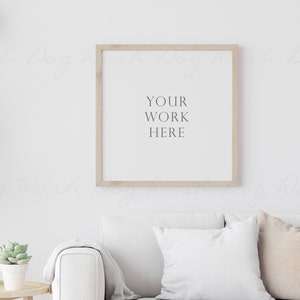 May include: A white couch with two pillows and a throw blanket in a living room with a wooden frame picture on the wall. The picture has the text "YOUR WORK HERE" on a white background.