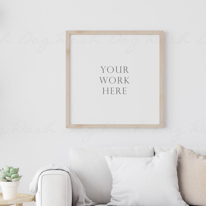 May include: A white couch with two pillows and a throw blanket in a living room with a wooden frame picture on the wall. The picture has the text "YOUR WORK HERE" on a white background.