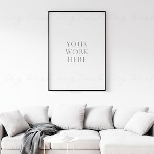 Może przedstawiać: Biała kanapa z szarymi poduszkami i czarnym kocem. Czarny obraz w ramie wisi na ścianie nad kanapą. Obraz zawiera tekst "YOUR WORK HERE".