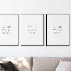 May include: Three black framed posters with white backgrounds and the text "Your work here" in the center of each poster. The posters are hanging on a white wall above a light gray couch.