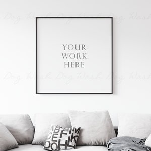 以下が含まれることがあります： 白い壁に「YOUR WORK HERE」という文字が書かれた白い額縁の絵が飾られています。その下には、グレーのソファがあり、白いクッションが置かれています。クッションの一つには、黒い文字で「ABEIM CEFHK DOHL」と書いてあります。