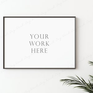 May include: A black framed picture mockup with the text "YOUR WORK HERE" on a white wall with a green plant in the corner.