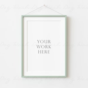 Puede incluir: Un marco de imagen verde claro colgado en una pared blanca. El marco está vacío y tiene el texto "YOUR WORK HERE" escrito en el centro.