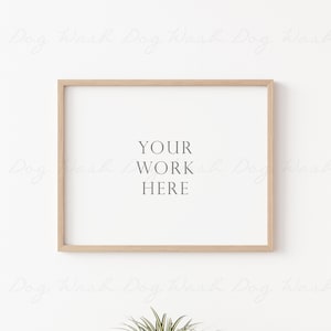 Può includere: Una cornice in legno chiaro con un passepartout bianco e uno sfondo bianco. Il testo "YOUR WORK HERE" è stampato al centro della cornice.