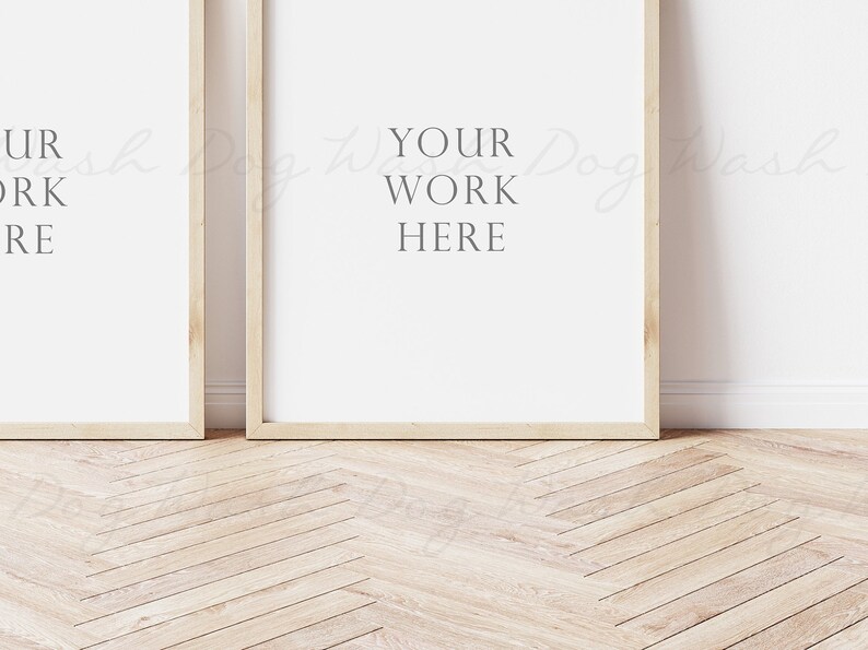 May include: Two wooden framed posters with white backgrounds, leaning against a white wall. The poster on the right has the text "YOUR WORK HERE" printed on it.