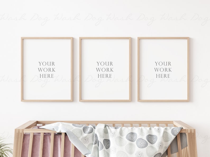 May include: Three wooden picture frames with white mats and the text "YOUR WORK HERE" in each frame. The frames are hanging on a white wall above a wooden crib with a white and gray patterned blanket.