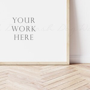 May include: A white framed poster mockup with the text "YOUR WORK HERE" on a white wall with a wood floor.