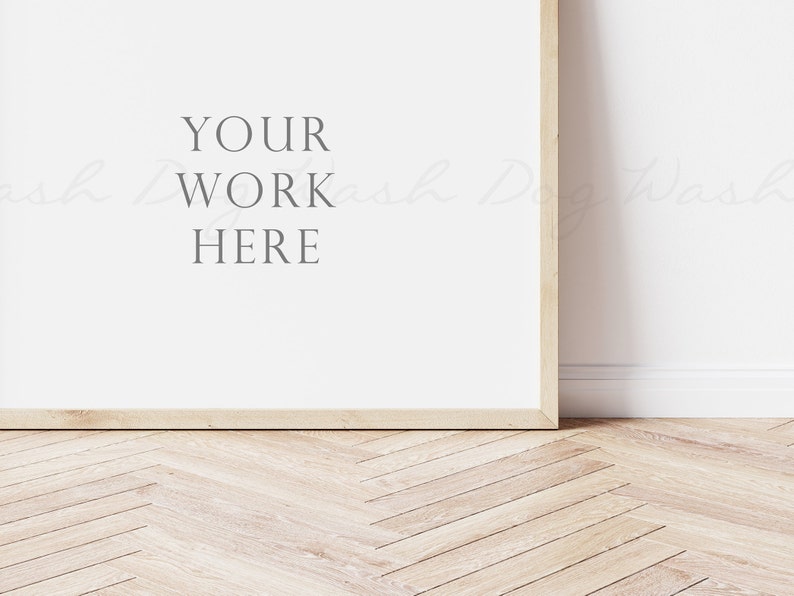 May include: A white framed poster mockup with the text "YOUR WORK HERE" on a white wall with a wood floor.
