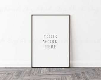 Könnte beinhalten: Ein schwarzer, rechteckiger Bilderrahmen lehnt an einer weißen Wand. Der Druck hat einen weißen Hintergrund mit dem Text "YOUR WORK HERE" in der Mitte. Der Boden ist ein hellgraues Fischgrätmuster.