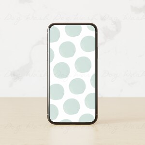 May include: A smartphone with a white background and a pattern of light blue circles. The phone is on a light wood surface.