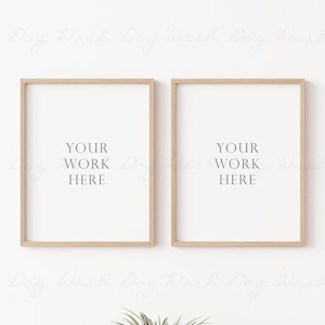 May include: Two light wood picture frames with white mats and the text "YOUR WORK HERE" in each frame. The frames are hanging on a white wall.