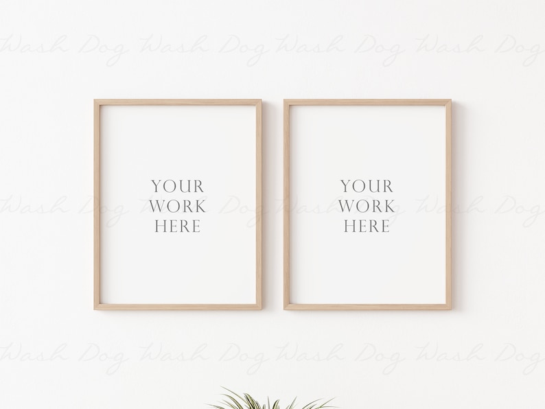 May include: Two light wood picture frames with white mats and the text "YOUR WORK HERE" in each frame. The frames are hanging on a white wall.