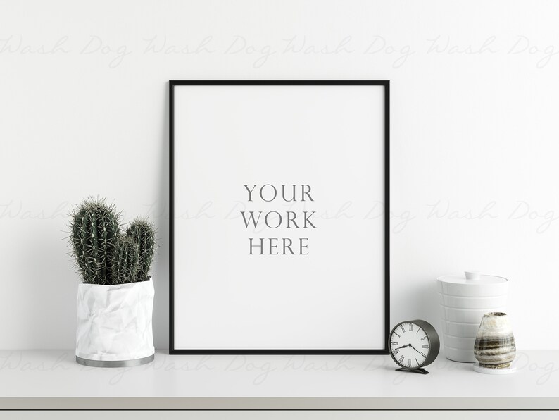 K&ouml;nnte beinhalten: Ein schwarz gerahmter Druck mit dem Text "YOUR WORK HERE" auf wei&szlig;em Hintergrund. Ein Kaktus in einem wei&szlig;en Topf, eine kleine schwarze Uhr und dekorative Gegenst&auml;nde befinden sich auf einer wei&szlig;en Oberfl&auml;che.
