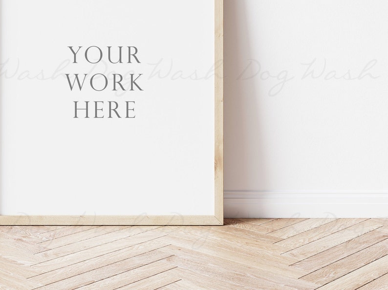 May include: A white framed poster with the text "YOUR WORK HERE" on a white wall with a wood floor.