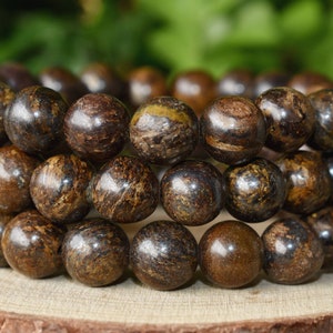 Puede incluir: Un brazalete hecho de cuentas de madera marrón oscuro con un patrón moteado. Las cuentas son redondas y lisas, y están enhebradas en un cordón.