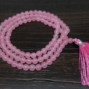 May include: A pink rose quartz mala with a pink tassel. The mala is made of round beads and is strung on a thin cord.