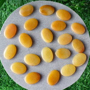 May include: A collection of 18 smooth, oval-shaped yellow citrine stones. The stones are arranged on a gray surface.