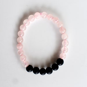 May include: A pink and black beaded bracelet. The bracelet is made with pink rose quartz beads and black lava rock beads.