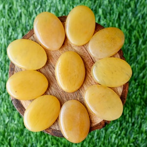 May include: A collection of ten smooth, oval-shaped yellow citrine stones arranged in a circle on a wooden surface. The stones are polished and have a translucent appearance.