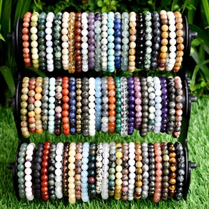 May include: A display of colorful gemstone bracelets, each made with different types of beads. The bracelets are arranged in three rows on a black stand.