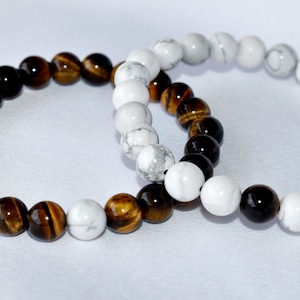 May include: Two beaded bracelets, one with brown and gold tiger's eye beads and the other with white howlite beads.