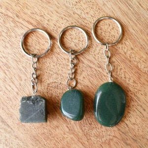 Puede incluir: Tres llaveros de piedra verde con anillos y cadenas plateados. Las piedras tienen diferentes formas, una es un rectángulo, otra es un rectángulo redondeado y la última es un óvalo redondeado.