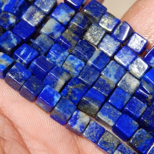 Può includere: Primo piano di un filo di perline quadrate di lapislazzuli. Le perline sono di un blu intenso con macchie d'oro e bianco. Le perline sono infilate, pronte per la creazione di gioielli.