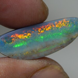 Op de afbeelding: Een blauwgrijze opaal edelsteen met een regenboog van kleuren, waaronder rood, oranje, geel, groen en blauw. De opaal is ovaalvormig en heeft een glad, gepolijst oppervlak.