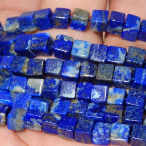 Puede incluir: Una taza de cerámica blanca con asa negra y el texto "But First, Coffee" en negrita negra. La taza se encuentra sobre un fondo borroso, sugiriendo un ambiente acogedor.