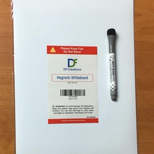 May include: A white magnetic whiteboard with a red and white label that says "Please Keep Flat Do Not Bend" and "Df Creations Magnetic Whiteboard 34 x 24 cm". The label also includes a barcode and the text "Made in China". A warning label is below the barcode. A white dry erase marker with a black cap is on the right side of the image.