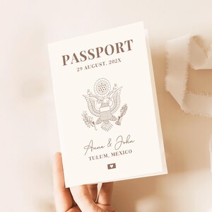 May include: A cream-colored passport-style booklet featuring brown text that reads PASSPORT, 29 AUGUST, 202X, Anna & John, and TULUM, MEXICO. A brown line-art illustration of the Great Seal of the United States and a small heart icon are centered.