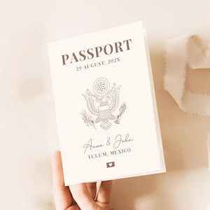 Puede incluir: Pasaporte color crema con la palabra "PASSPORT" en letras marrones. La fecha "29 AGOSTO, 202X" está impresa debajo. Un emblema de águila está centrado, con los nombres "Anna & John" y "TULUM, MEXICO" debajo. Un pequeño icono de corazón está en la parte inferior.