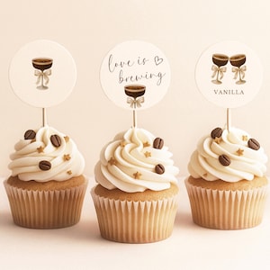 May include: Three cupcakes with white frosting, coffee bean and star decorations, and round toppers. The toppers feature coffee cup illustrations and the phrases "Love is Brewing" and "Vanilla".